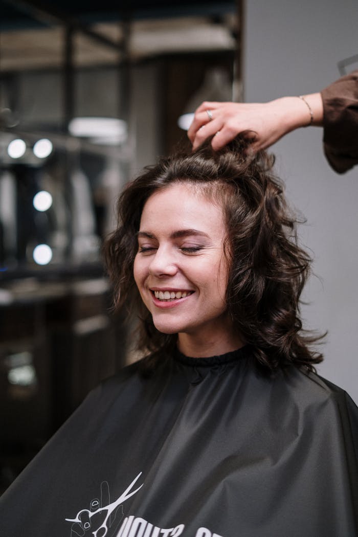 Smiling woman with closed eyes in a hair salon, receiving hairstyling service.